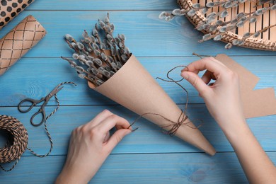 Photo of Woman making beautiful bouquet of pussy willow branches at light blue wooden table, top view