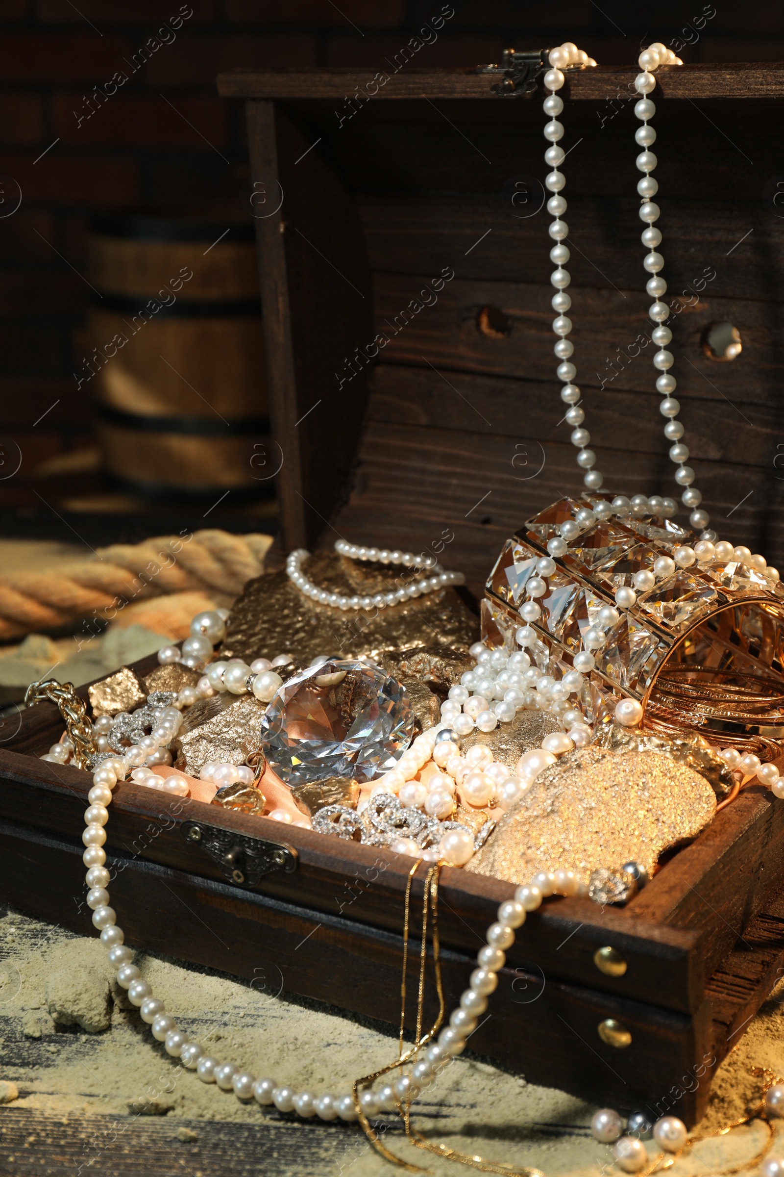 Photo of Chest with treasures and scattered sand on wooden table