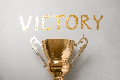 Gold trophy cup and word VICTORY made with confetti on light grey stone background, flat lay