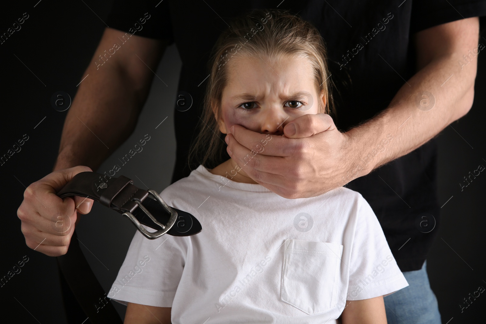 Photo of Man with belt covering scared little girl's mouth on black background. Domestic violence