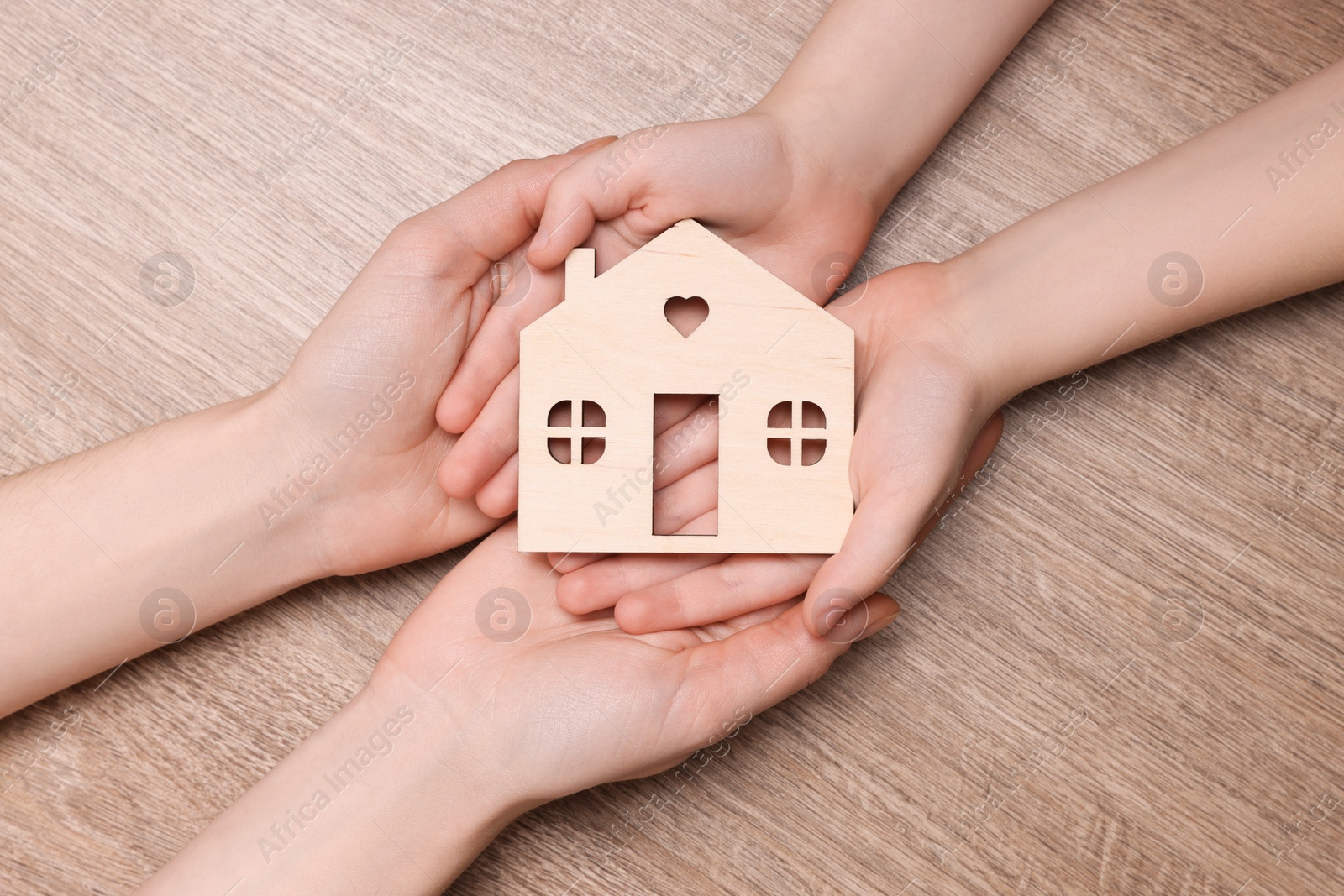 Photo of Home security concept. Woman with her little child holding house model at wooden table, top view