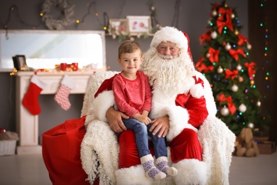 Little boy sitting on authentic Santa Claus' lap indoors