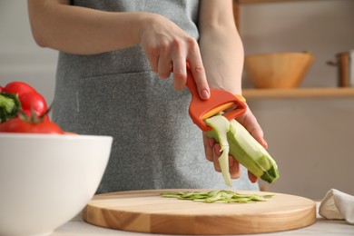 Photo of Woman peeling fresh zucchini at table in kitchen, closeup