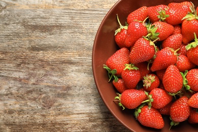 Plate with fresh ripe strawberries on wooden background, top view