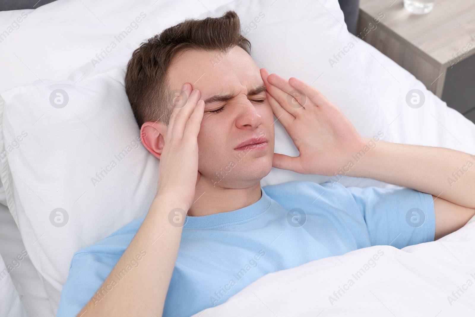 Photo of Sad man suffering from headache in bed indoors