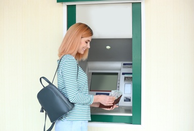 Beautiful woman with money near cash machine outdoors