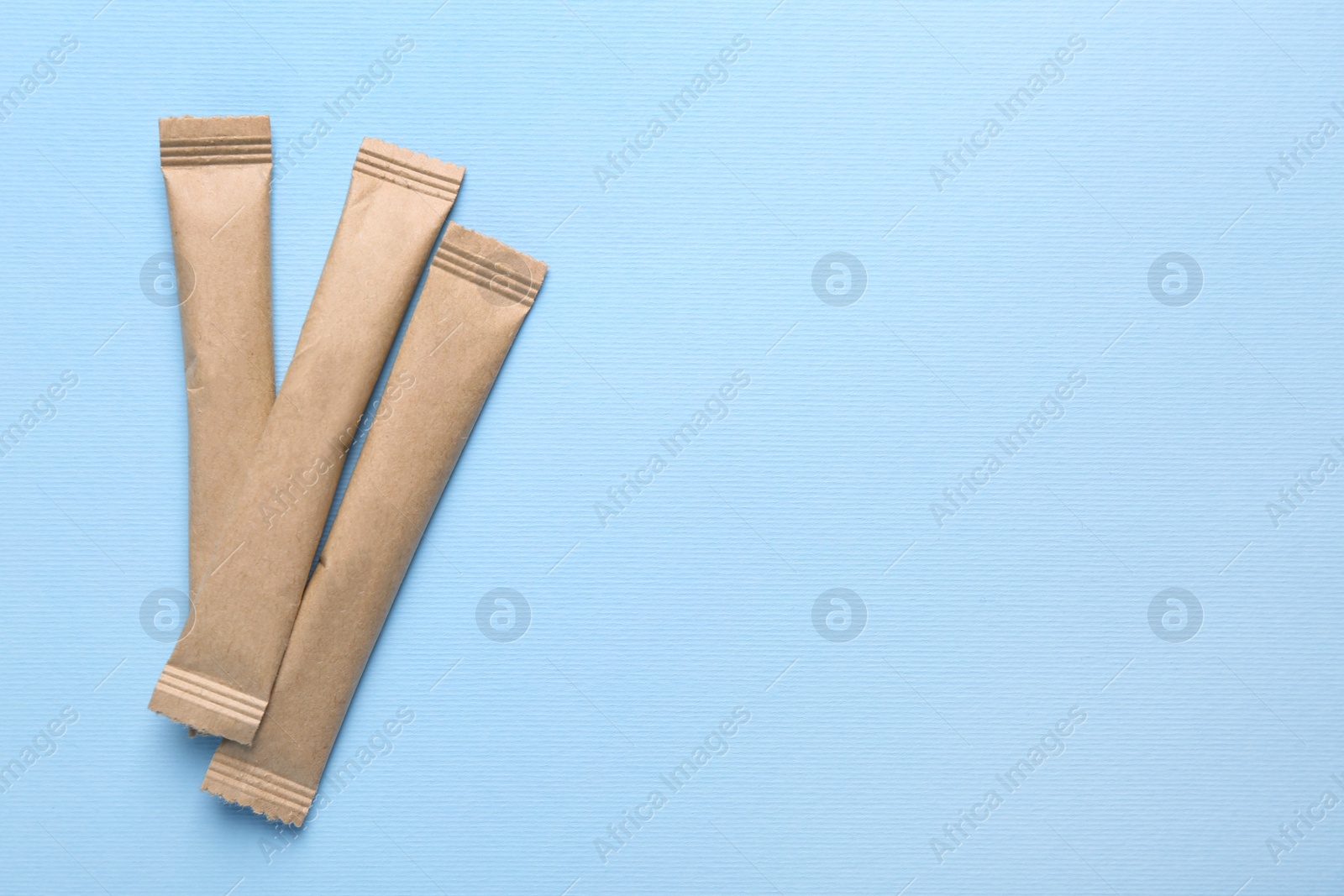 Photo of Beige sticks of sugar on light blue background, flat lay. Space for text