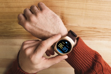 Image of Man measuring oxygen level with smartwatch at wooden table, top view