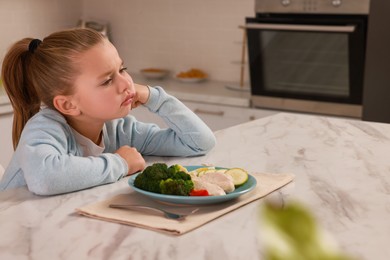 Photo of Cute little girl refusing to eat dinner in kitchen, space for text