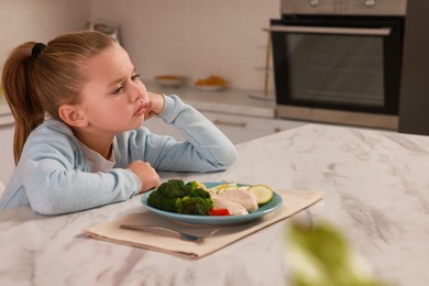 Cute little girl refusing to eat dinner in kitchen, space for text