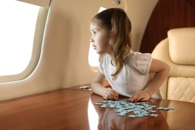 Photo of Cute little girl solving jigsaw puzzle at table in airplane during flight