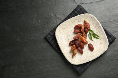 Plate with sweet dried dates and leaves on black table, top view. Space for text