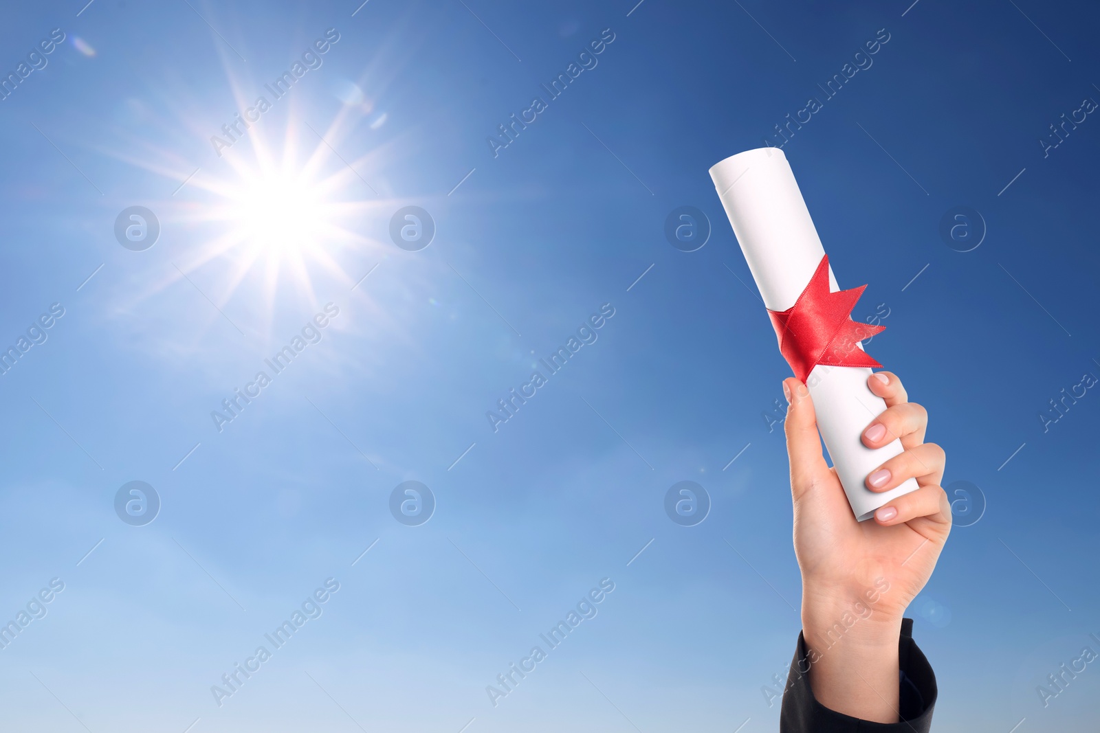 Image of Graduated student holding diploma against blue sky on sunny day, closeup