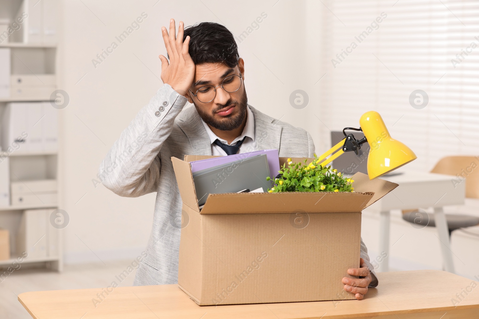 Photo of Unemployment problem. Frustrated man with box of personal belongings at desk in office