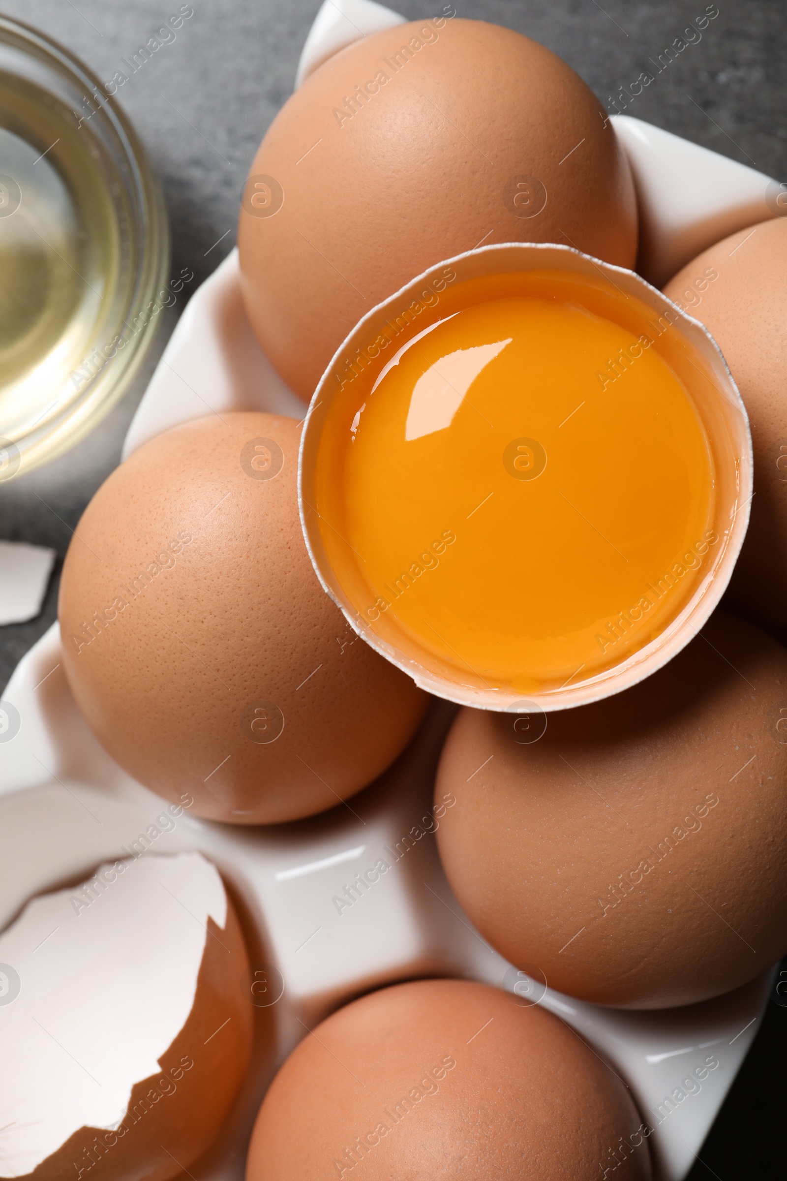 Photo of Box of whole and cracked chicken eggs on grey table, flat lay