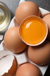 Box of whole and cracked chicken eggs on grey table, flat lay