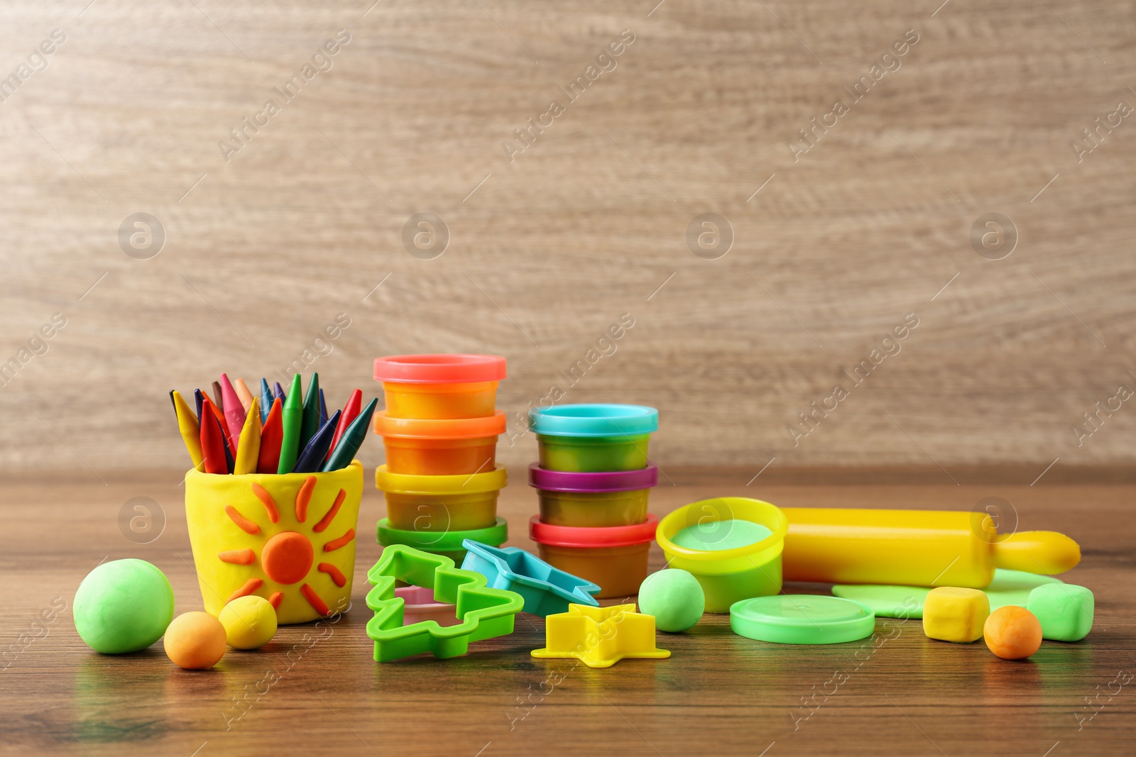 Photo of Set of bright play dough with tools and colorful pencils on wooden table