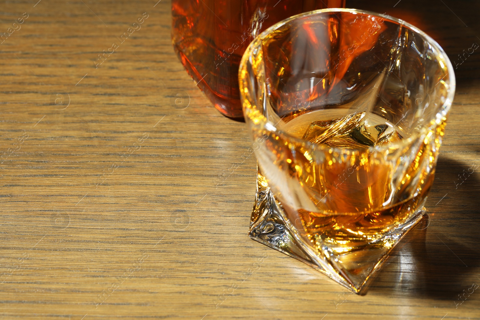 Photo of Whiskey in glass on wooden table, closeup. Space for text