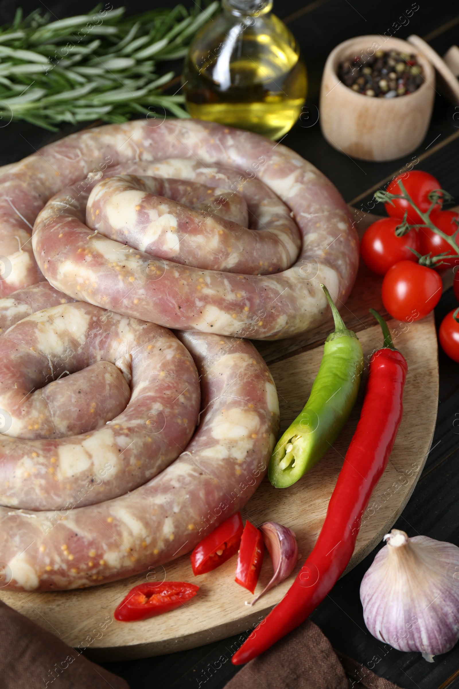 Photo of Raw homemade sausages, spices and other products on dark wooden table, closeup