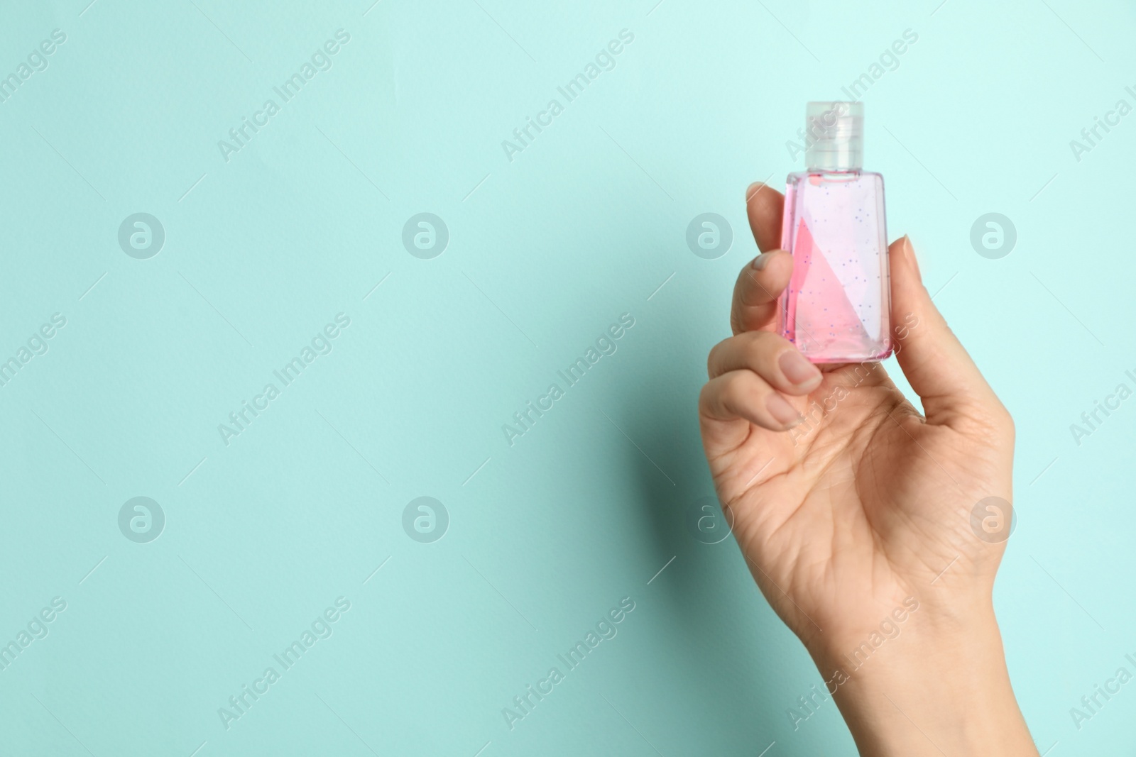 Photo of Woman holding antiseptic gel on light blue background, closeup. Space for text