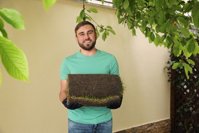 Photo of Young man holding rolled grass sod at backyard