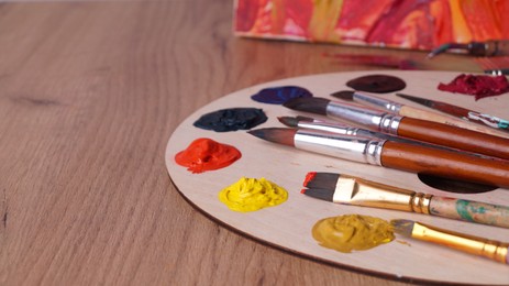 Artist's palette with many colorful paints and brushes on wooden table, closeup. Space for text