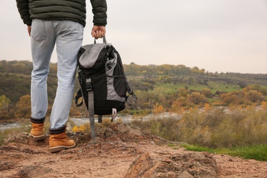 Traveler with backpack on steep cliff near mountain river, closeup. Autumn vacation