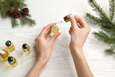 Woman holding bottle with pine essential oil at white wooden table, top view