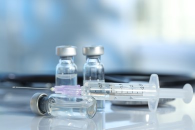 Glass vials, syringe and stethoscope on white table, closeup