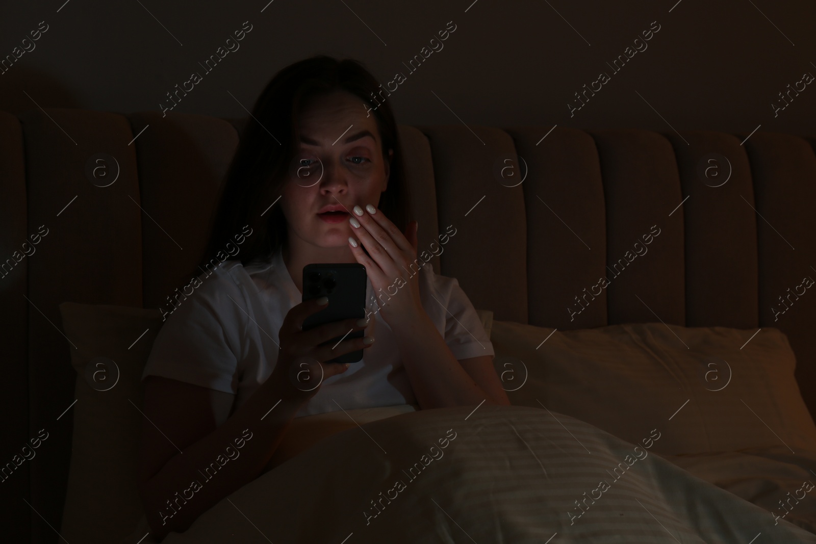 Photo of Woman using smartphone in bed at night. Internet addiction