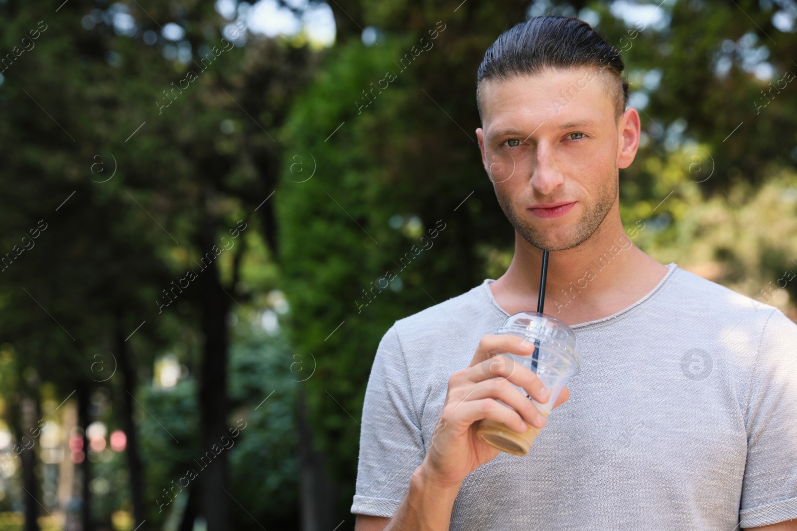 Photo of Handsome young man drinking coffee in park, space for text