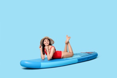 Photo of Happy woman resting on SUP board against light blue background