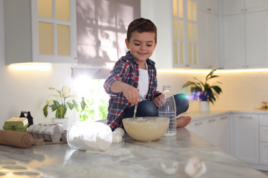 Photo of Cute little boy cooking dough on table in kitchen