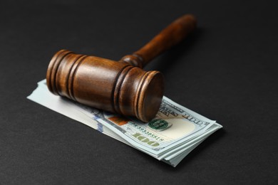 Photo of Law gavel with stack of dollars on black table, closeup