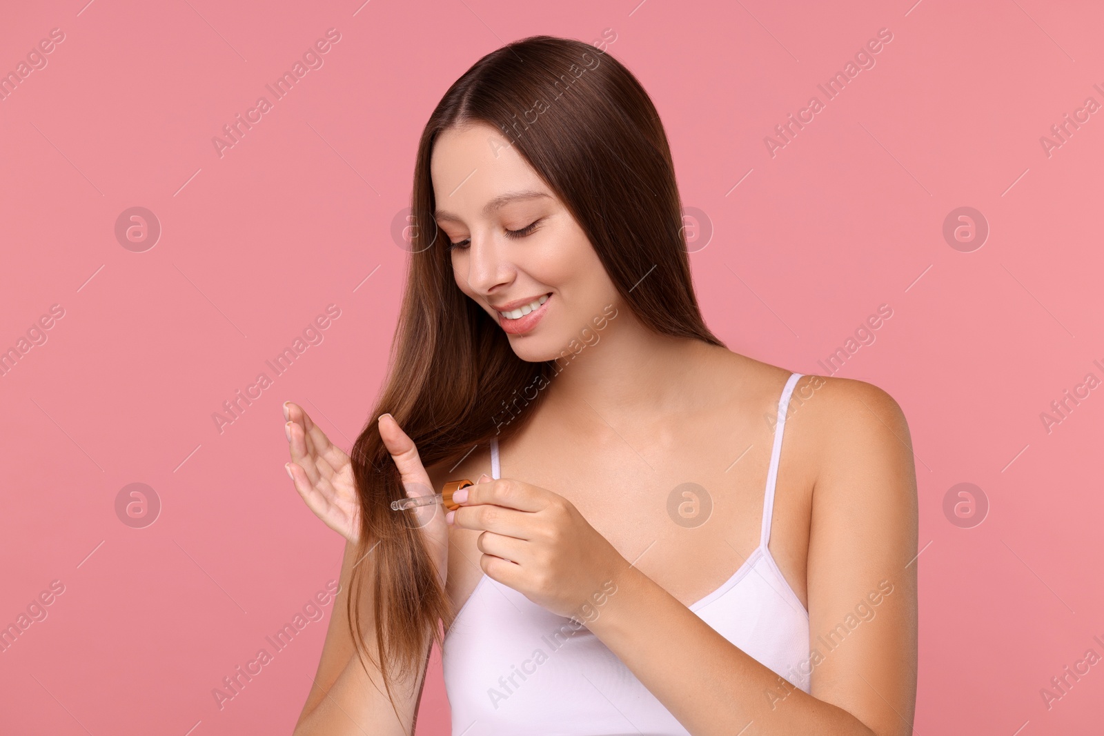 Photo of Beautiful woman applying serum onto hair on pink background