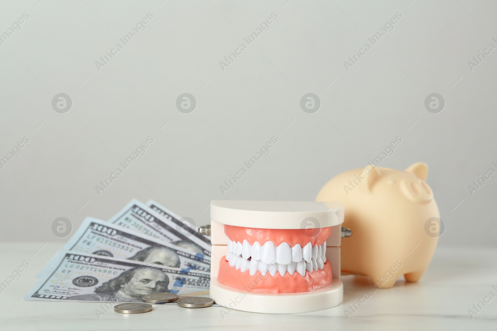 Photo of Educational dental typodont model, piggy bank and money on white table. Expensive treatment