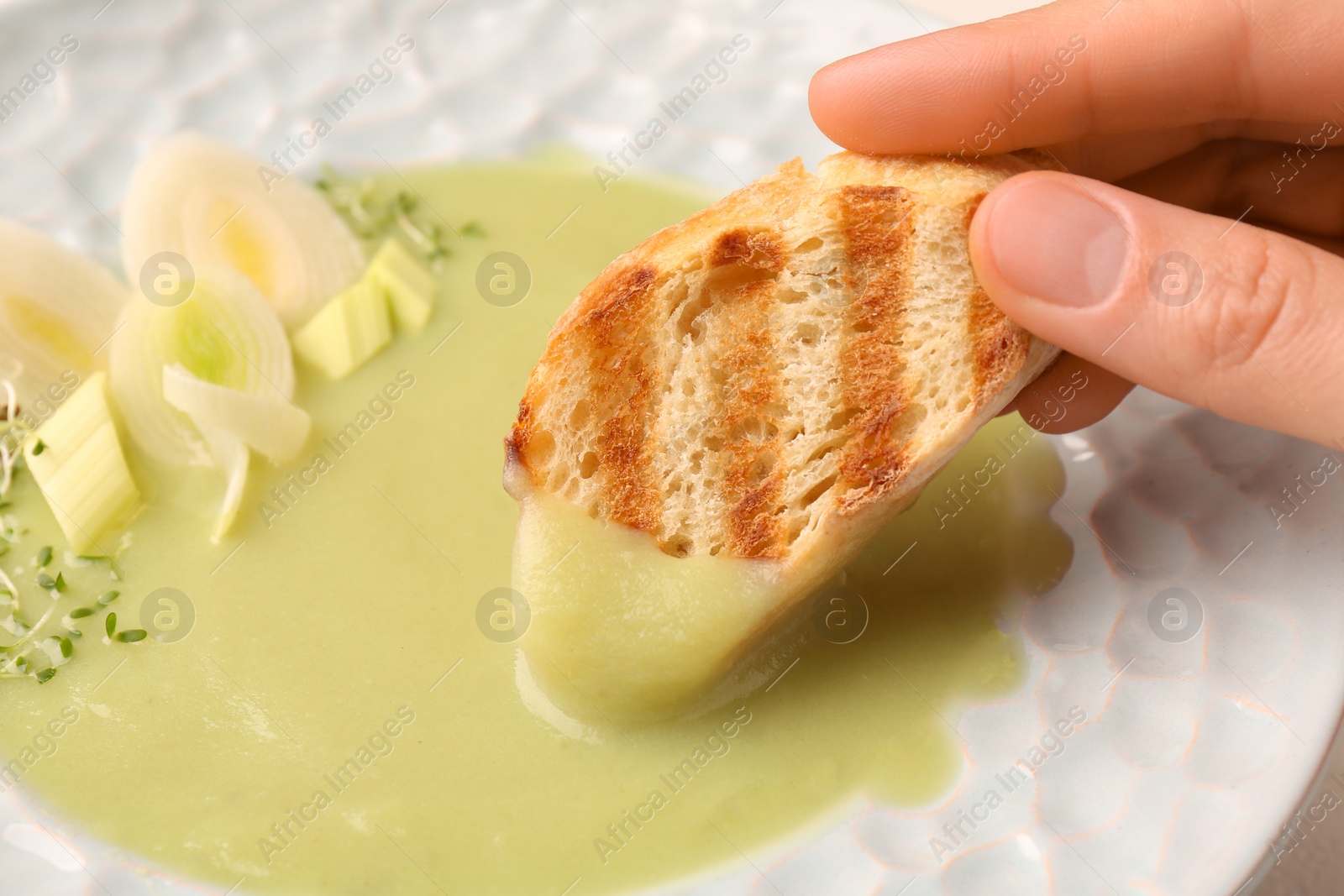 Photo of Woman dipping crouton into delicious leek soup, closeup