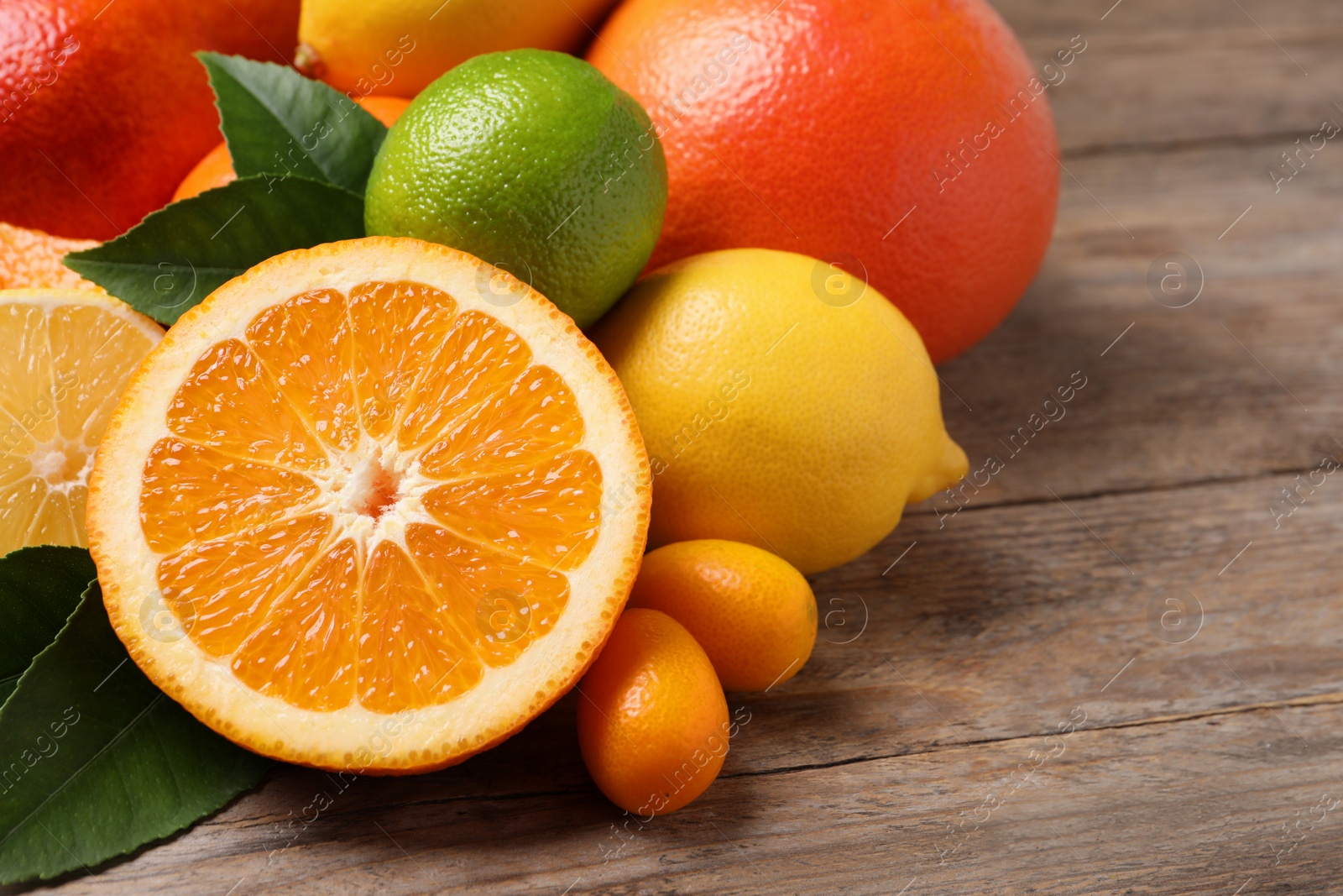 Photo of Fresh juicy citrus fruits with green leaves on wooden table