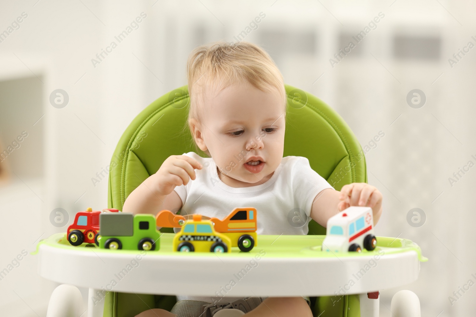 Photo of Children toys. Cute little boy playing with toy cars in high chair at home