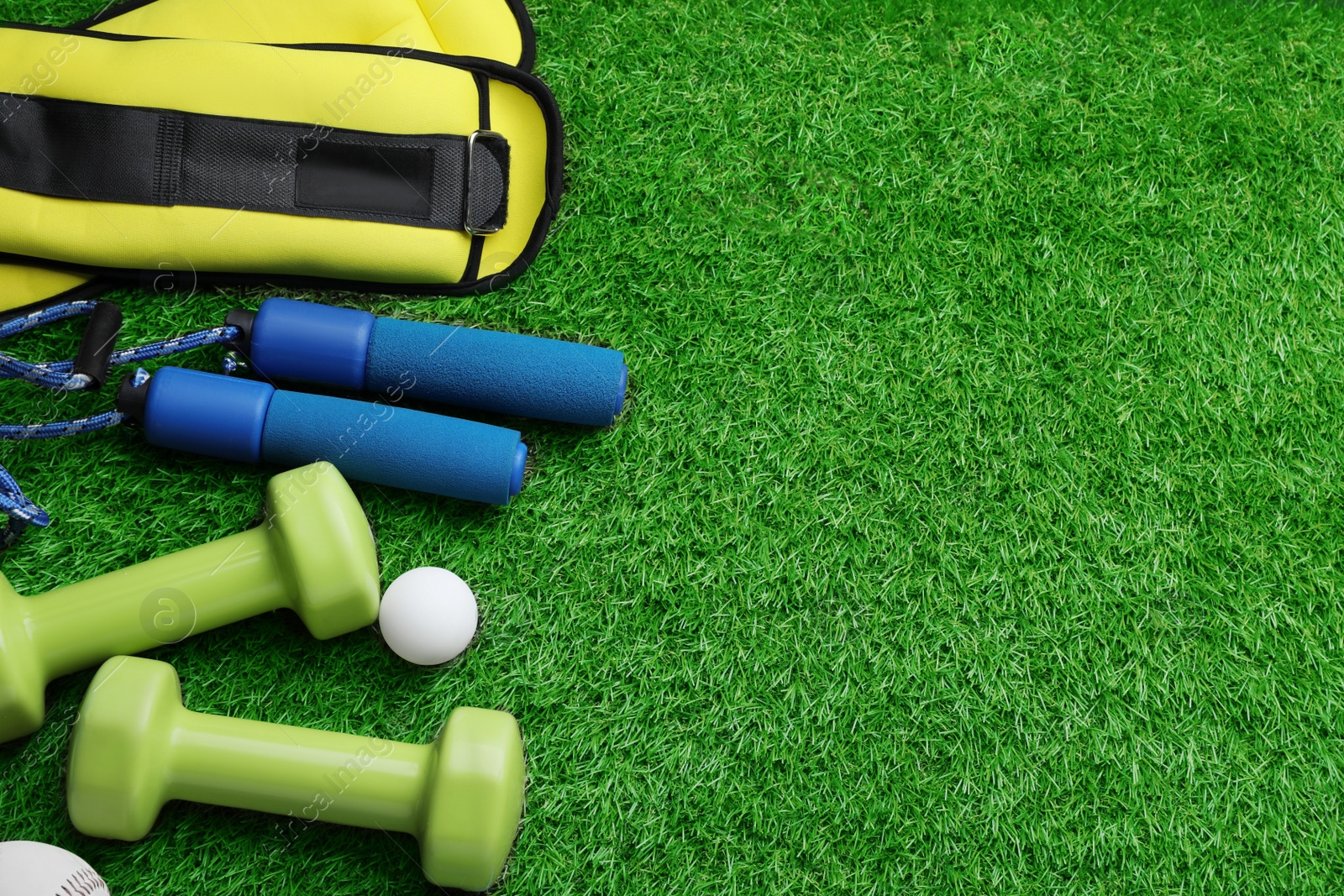 Photo of Set of different colorful sports equipment on green grass, above view. Space for text