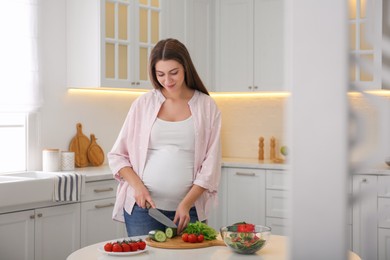 Photo of Young pregnant woman preparing vegetable salad at table in kitchen. Healthy eating