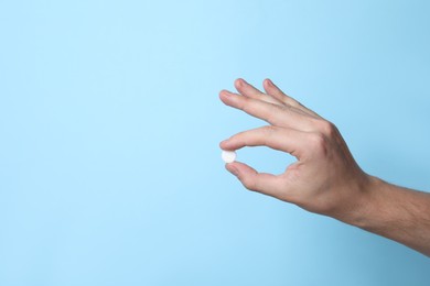 Photo of Man holding pill on light blue background, closeup. Space for text