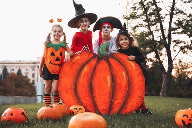 Photo of Cute little kids with decorative pumpkin wearing Halloween costumes in park