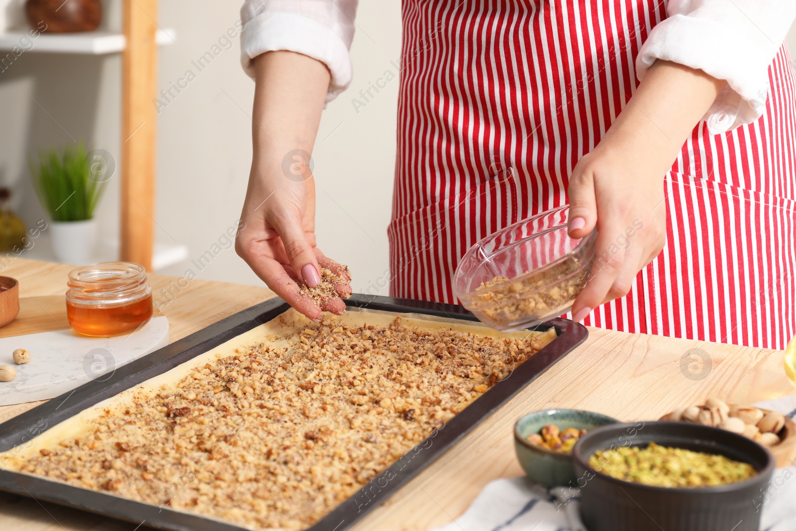 Photo of Making delicious baklava. Woman adding chopped nuts to dough at wooden table, closeup