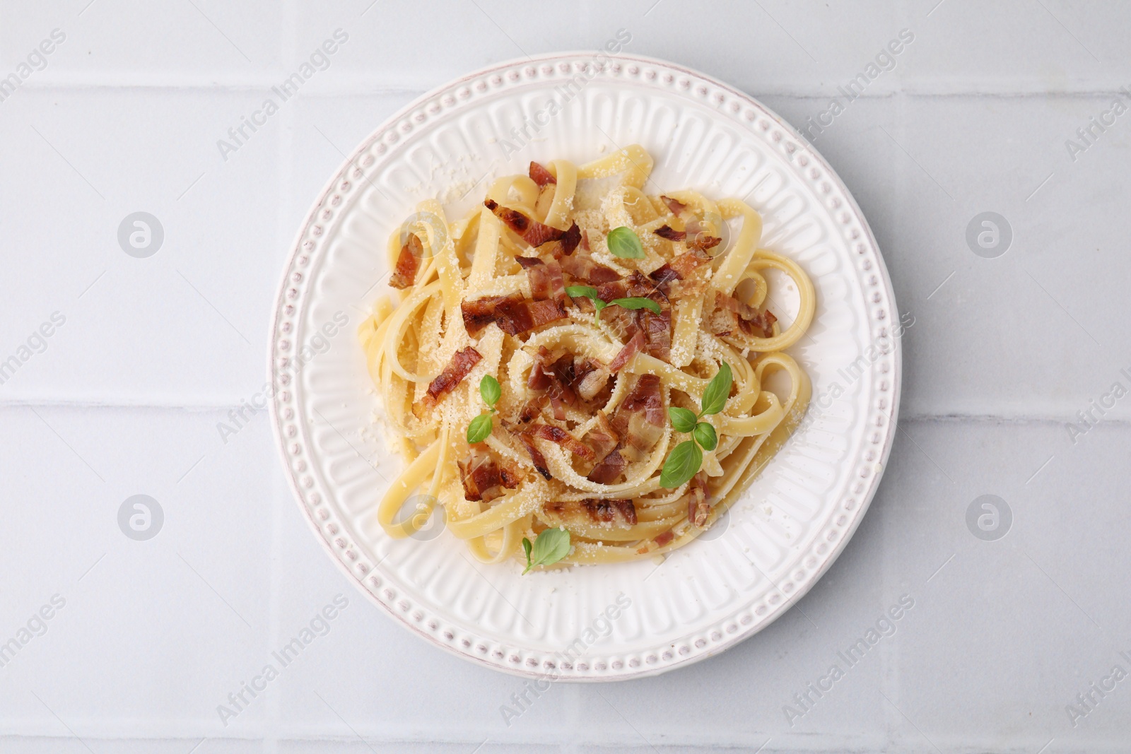 Photo of Tasty pasta with bacon and basil on white tiled table, top view