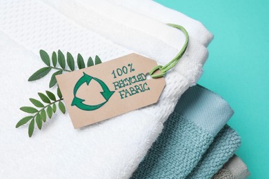 Photo of Stacked towels with recycling label and plant on turquoise background, closeup