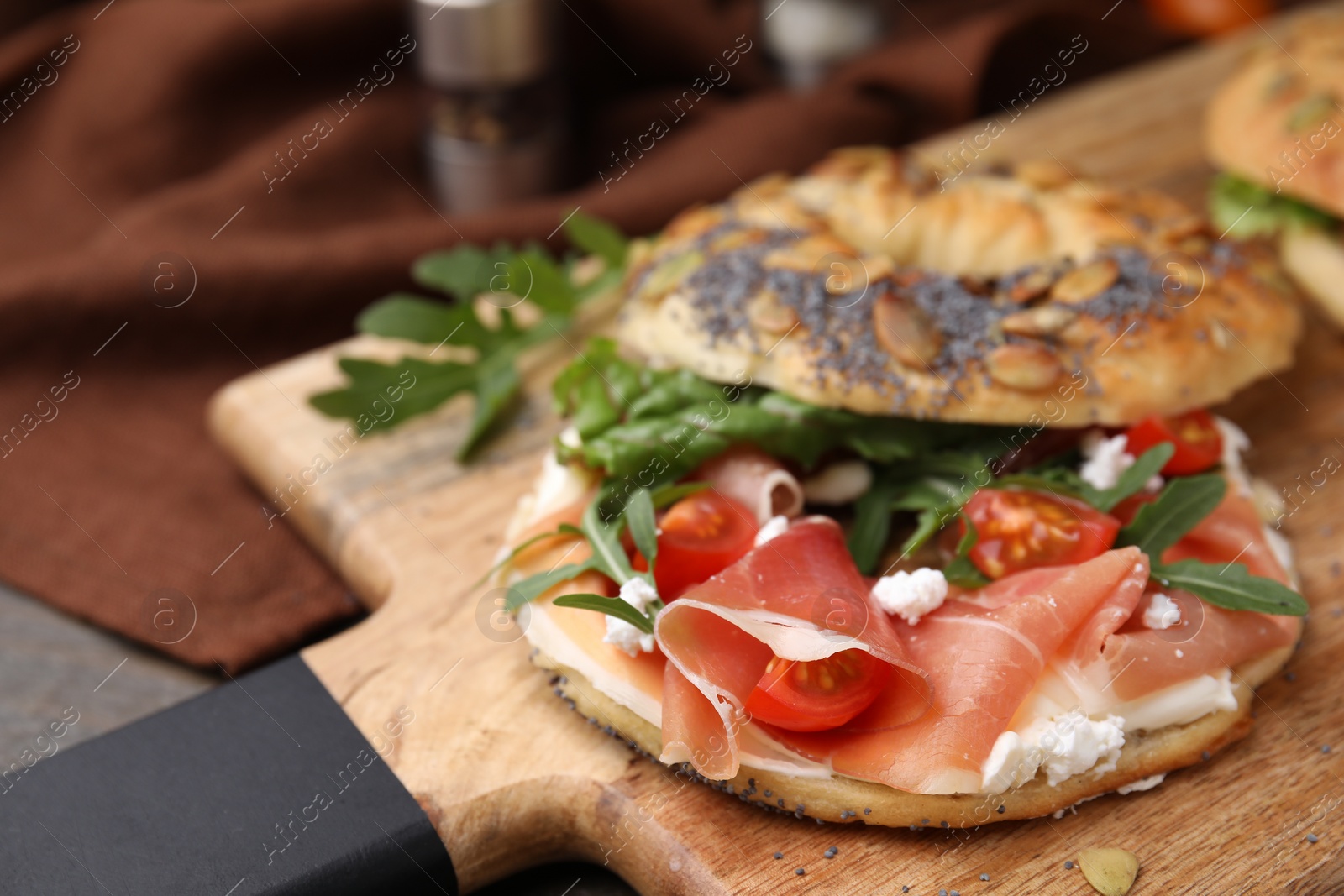 Photo of Tasty bagel with cured ham, cream cheese, tomatoes and arugula on table, closeup