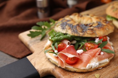 Photo of Tasty bagel with cured ham, cream cheese, tomatoes and arugula on table, closeup