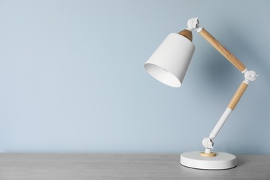 Stylish modern desk lamp on wooden table near white wall, space for text