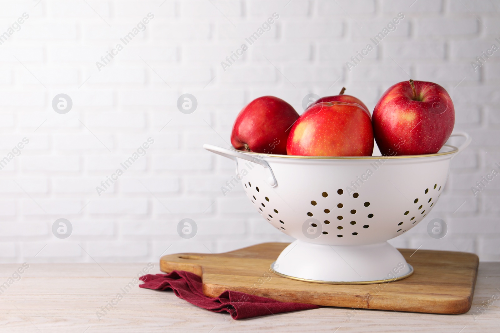 Photo of Fresh apples in colander on white wooden table. Space for text